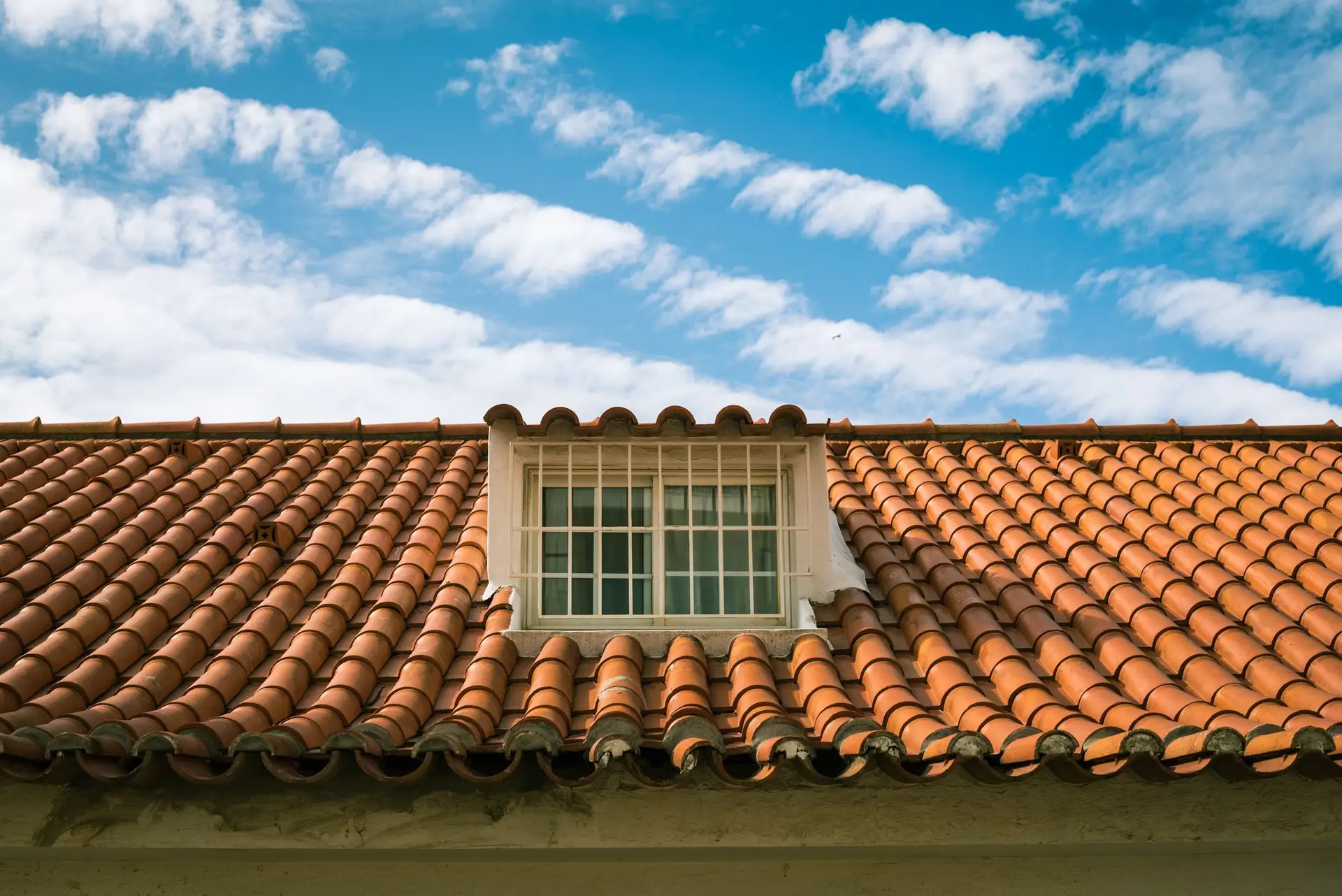 Terracotta tile roof with a dormer window under a blue sky
