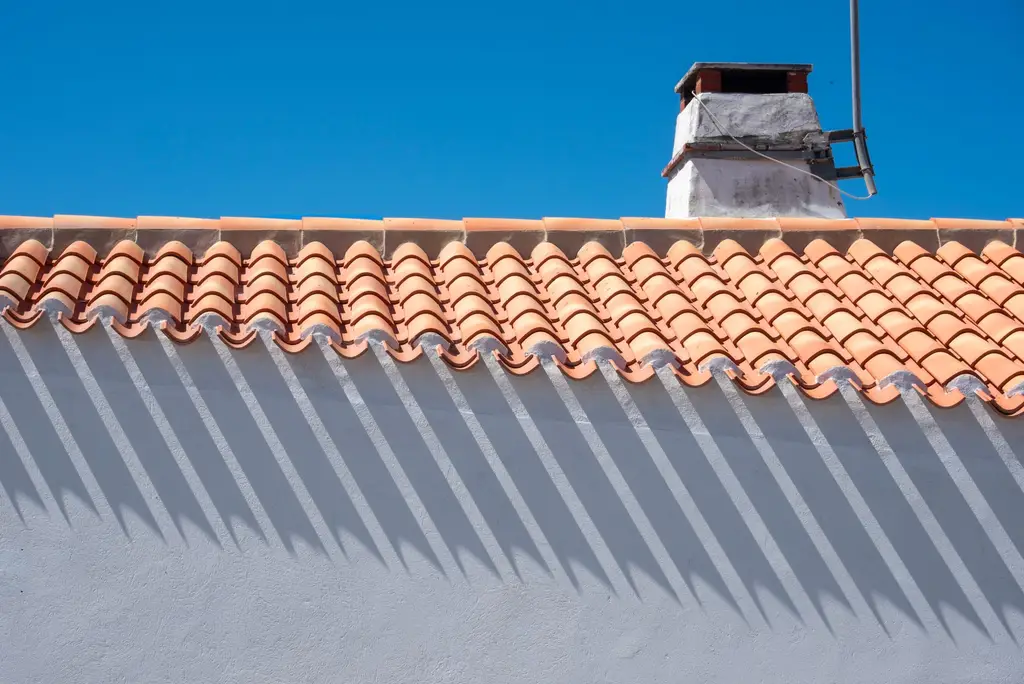 Barrel tile eave casting shadows on a white wall