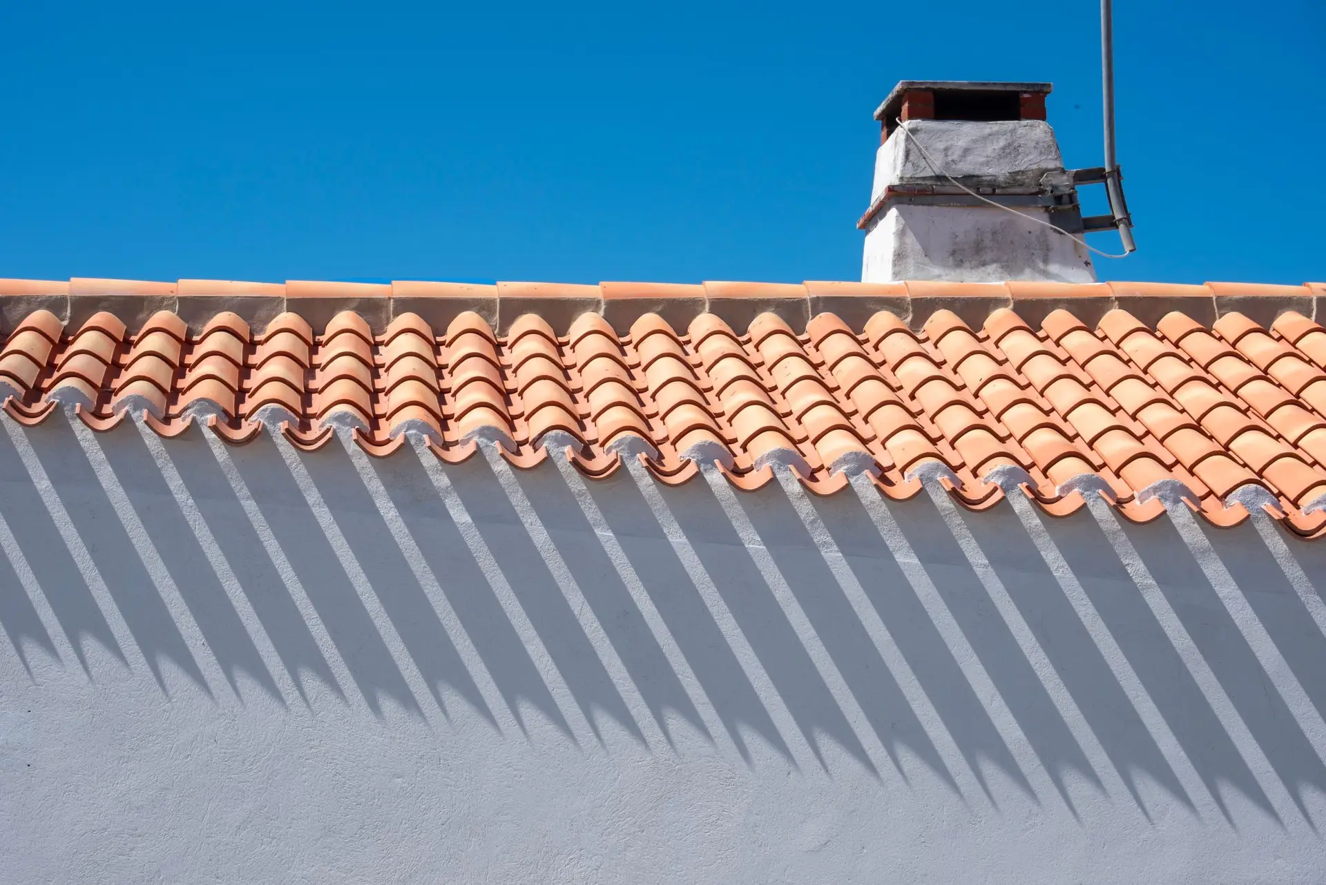 Barrel tile eave casting shadows on a white wall